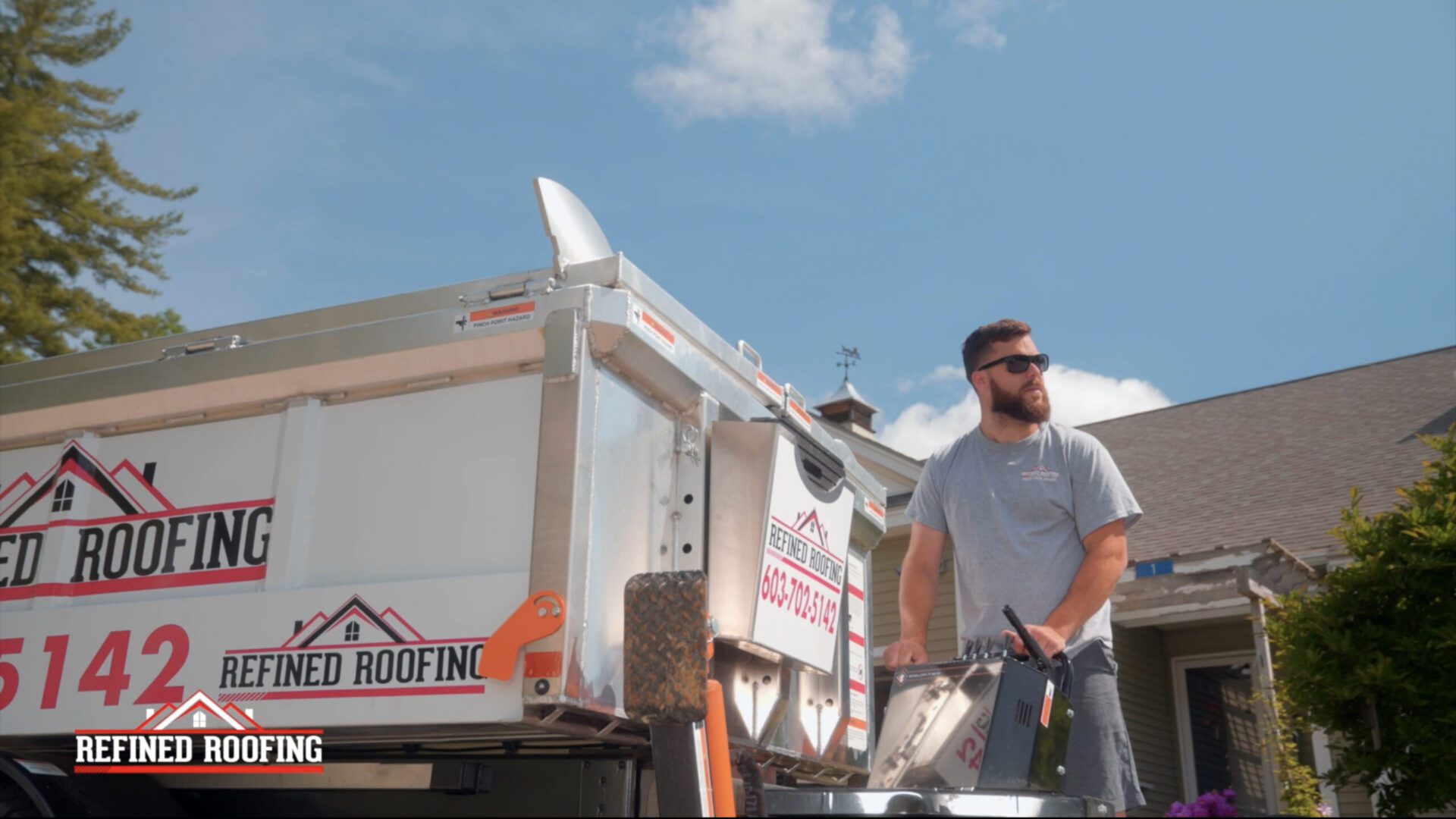 Worker standing beside roofing truck under blue sky