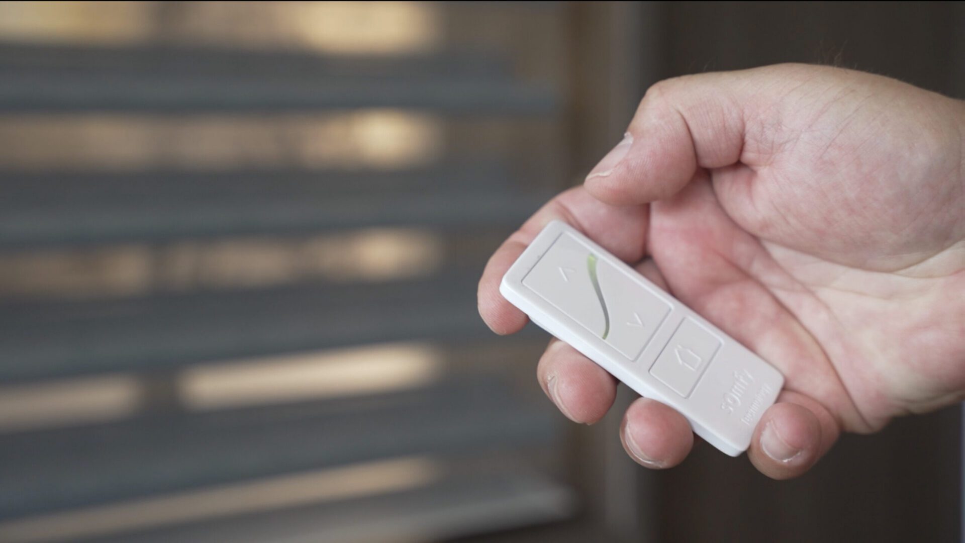 Hand holding white remote control near blinds