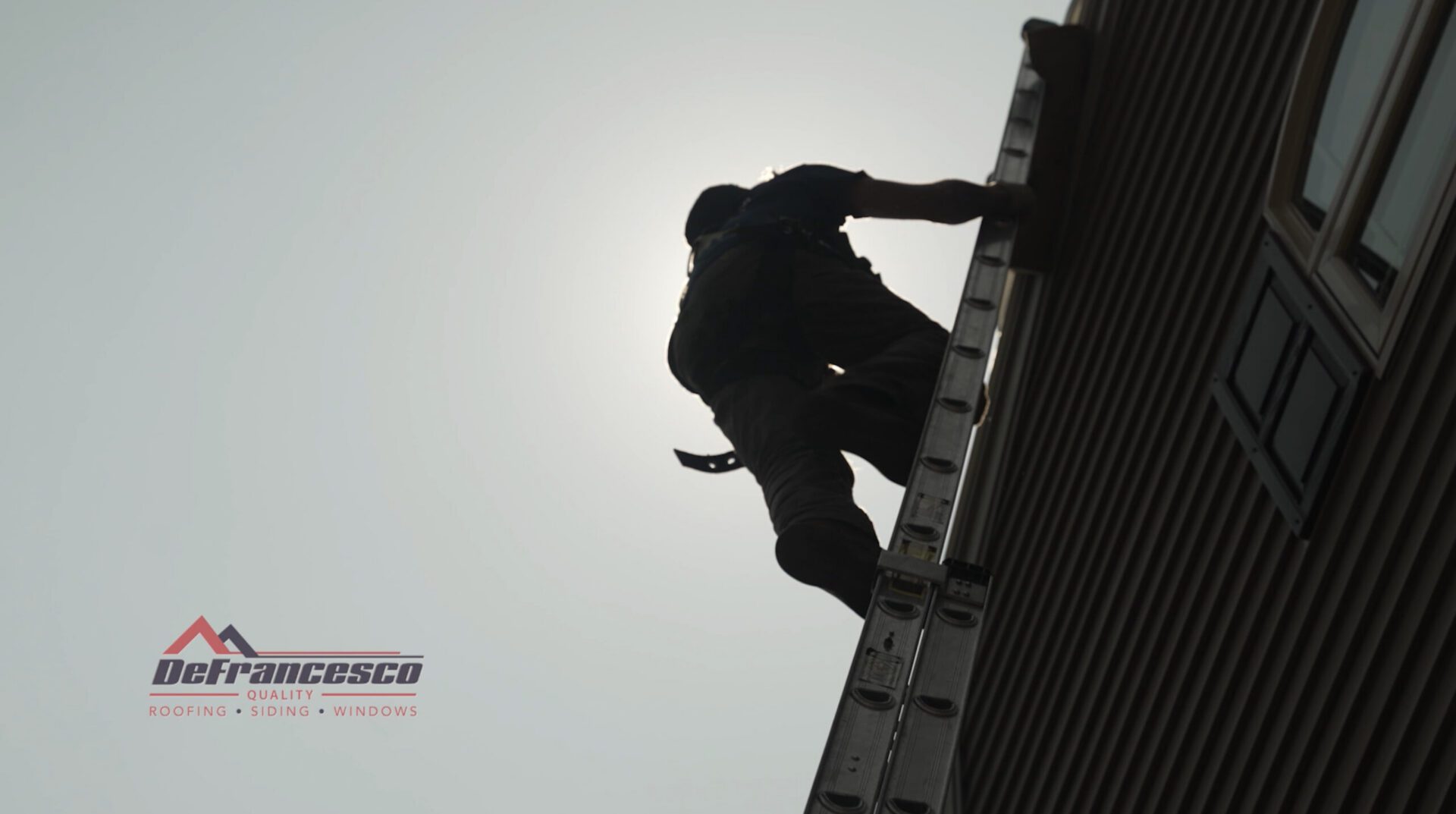 Silhouette roofer climbing ladder by house