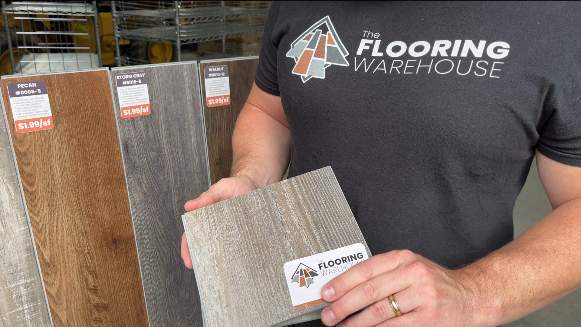 Person holding gray wood flooring sample in warehouse