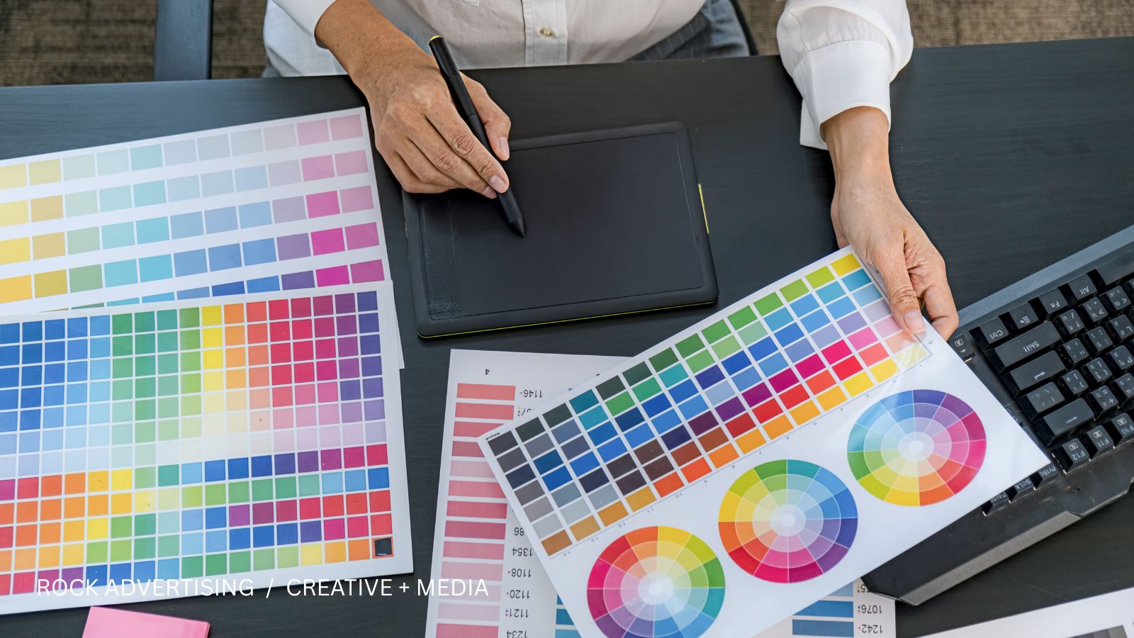 Designer working with a drawing tablet and printed color swatches