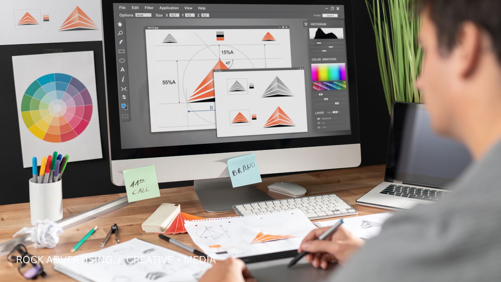 Designer sketching logo concepts beside a computer with brand color studies